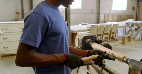 Woodturning craftsman shaping spindle on lathe in industrial woodworking workshop