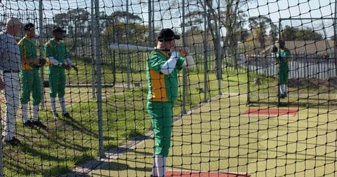 Cricket team practicing in batting nets wearing green and yellow uniforms