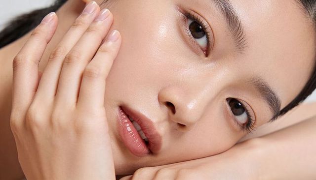Closeup female model touching cheek showcasing dewy skin and glossy lips for skincare ads