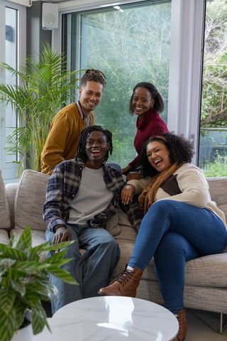 Diverse friends laughing and chatting on cozy sofa in bright modern living room with plants