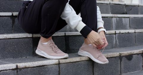 Senior woman tying light pink sneakers on outdoor urban steps for walking and fitness