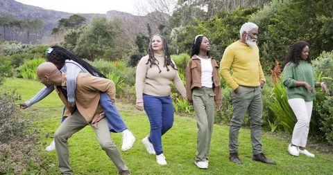 Multigenerational family strolling lush garden with father giving daughter piggyback, smiling