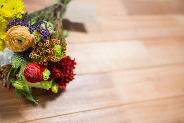 This image showcases a vibrant flower bouquet placed on a wooden surface. The mix of colorful flowers creates a lively and fresh atmosphere, making it perfect for use in floral arrangement promotions, nature-themed designs, or spring and summer event invitations. The rustic wooden background adds a natural and warm touch, suitable for home decor inspirations or gardening blogs.
