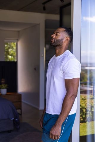 Mature african american man leaning against sliding glass door, relaxing on balcony