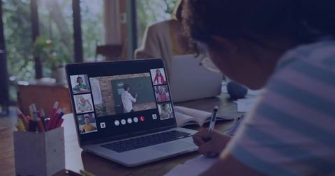 Child Writing Notes While Attending Live Virtual Classroom on Laptop at Home Desk