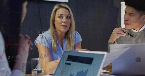 Female executive leading team meeting while reviewing graphs and analytics on laptops