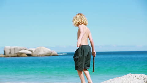 Blonde Child Exploring Beach with Stick Under Clear Sky