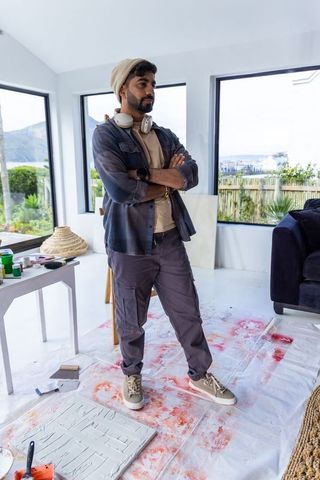 Indian artist standing in light-filled studio inspecting canvas and palette knife, creative space