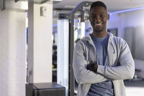 Smiling Confident African American Fitness Trainer Standing with Arms Crossed in Modern Gym