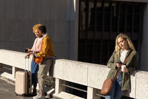 Young diverse adults waiting on urban terrace with suitcase, basketball, smartphones, coffee