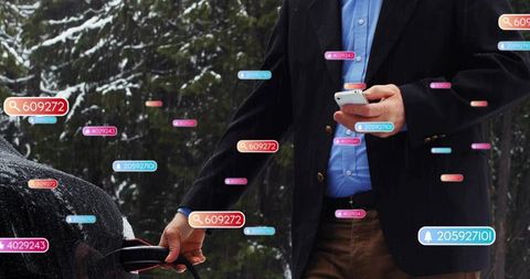Man in blazer charging electric car while checking smartphone with ar tags in snowy forest