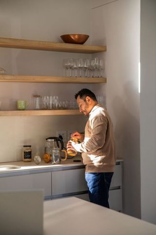 Asian man preparing morning coffee with french press in minimalist sunlit modern kitchen