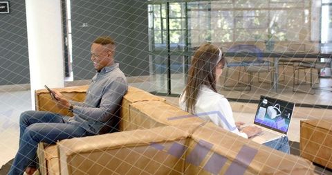 Back-to-back colleagues on brown sofa, woman editing 3d model, man checking phone