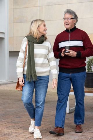 Senior couple walking and chatting in urban plaza holding takeaway coffee and bag
