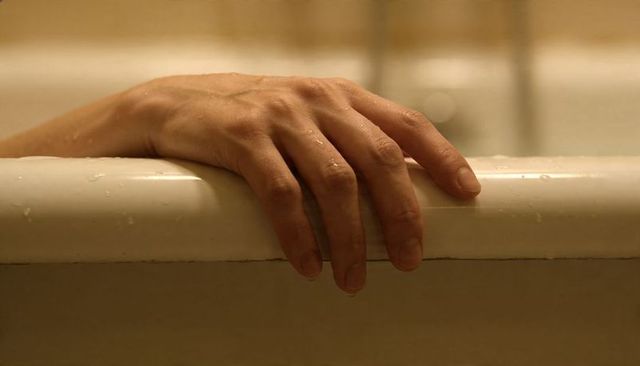 Resting wet hand draping over bathtub rim with water droplets closeup moody warm light