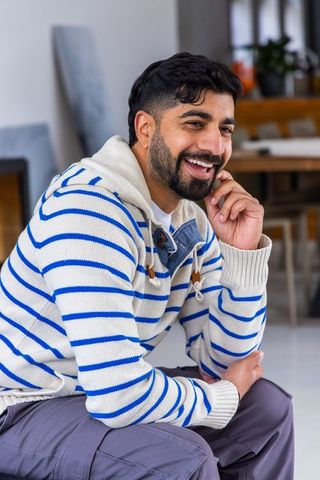 Smiling indian man relaxing in striped knit hooded sweater at home, contemporary lifestyle