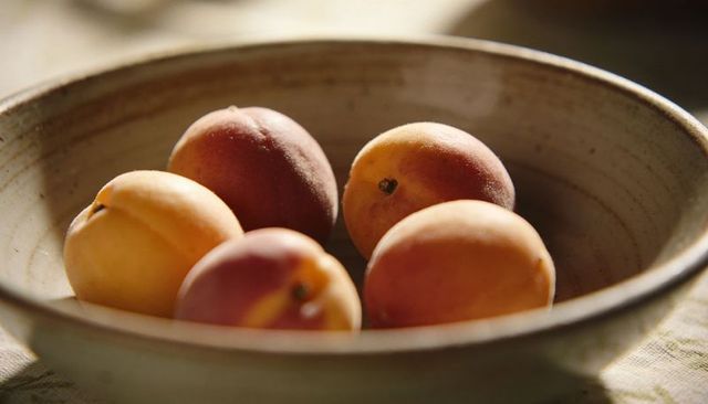 Rustic ceramic bowl holding five ripe apricots in warm natural window light