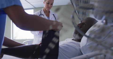 Hospital team monitoring vitals, nurse applying bp cuff to male patient while physician using tablet