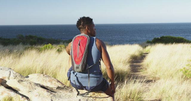 African American male is backpacking along a coastal trail, with ocean horizon visible in background. Exemplifies adventure, nature exploration, and relaxation. Suitable for themes around outdoor activities, travel promotion, personal journeys, and summer vacations.
