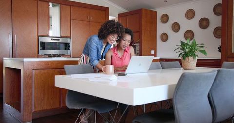 Diverse female couple collaborating on laptop at home office