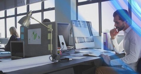 Focused businessman resting chin while viewing monitor in modern open-plan coworking office