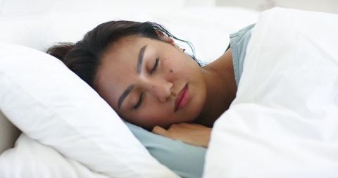 Mid adult asian woman sleeping peacefully on white duvet for restful bedroom lifestyle