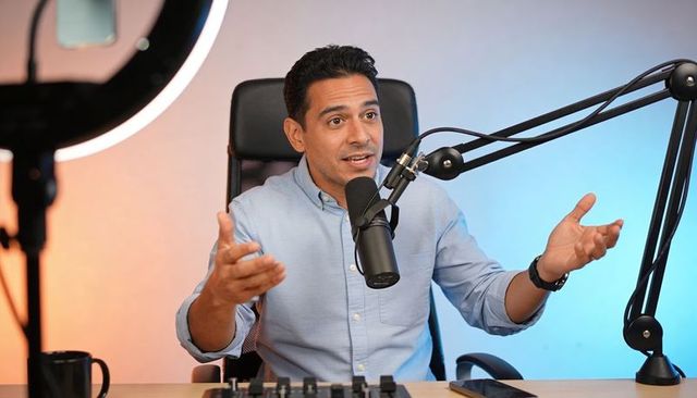 Male podcast host speaking and gesturing in home studio with microphone and ring light