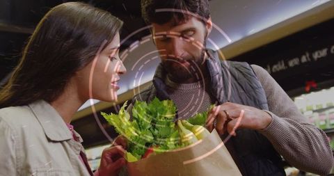 Couple inspecting fresh produce in grocery aisle holding paper bag of greens and fruit
