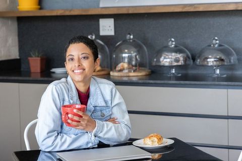 Smiling african american woman enjoying coffee and pastry in modern kitchen workspace