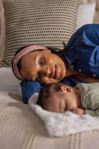 Mother resting beside sleeping baby on cozy bed, sharing tender close bonding moment
