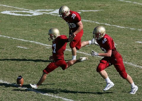 High School Football Kicker Delivering Powerful Kick During Game With Teammates Sprinting