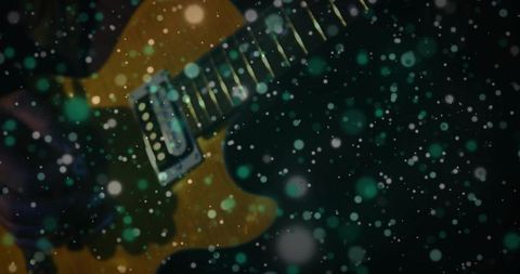 Yellow electric guitar leaning in moody lowlight with green bokeh particles, diagonal angle