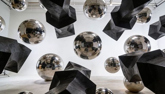 Suspending chrome spheres reflecting visitors among matte polyhedral blocks in gallery