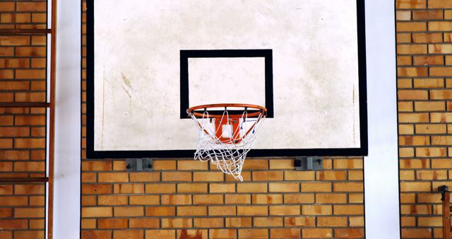 Empty indoor basketball hoop with brick wall background. Great for illustrating sports facilities, fitness activities, and gym environments. Suitable for content related to basketball, exercise, recreation, and sports equipment.