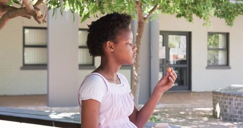 Teen girl sitting on bench under tree holding snack enjoying quiet courtyard moment