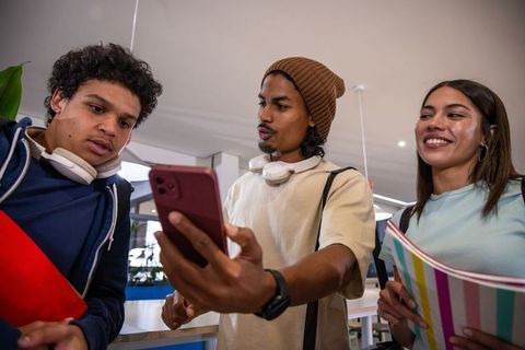 Multicultural students sharing smartphone while studying and collaborating in campus lounge
