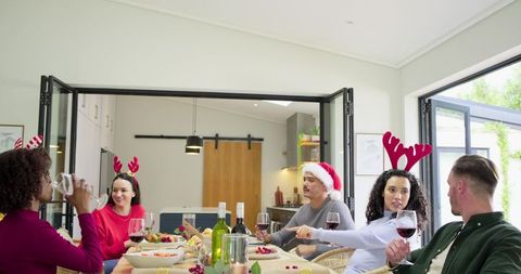 Friends celebrating holiday dinner with reindeer antlers and santa hat in modern kitchen