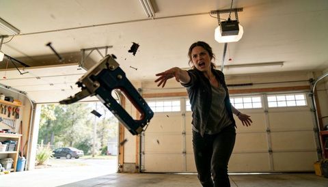 Throwing woman launching power nailer across garage, dramatic debris flying, tense action