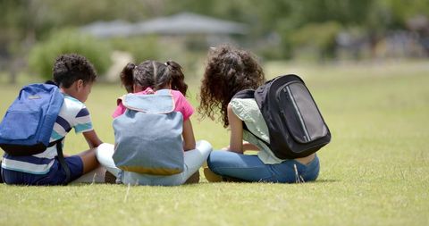 Children with Backpacks Sitting on Grass Engaged in Outdoor Activity - Download Free Stock Images Pikwizard.com