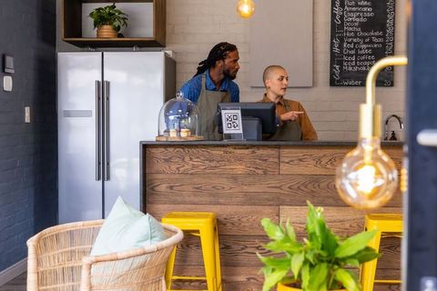 Diverse baristas pointing at pos terminal behind rustic wooden counter and pastries