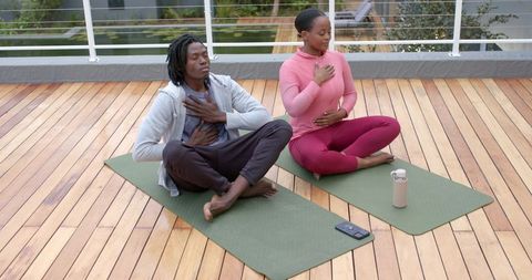 African american friends practicing breathwork and mindful breathing on rooftop yoga mats