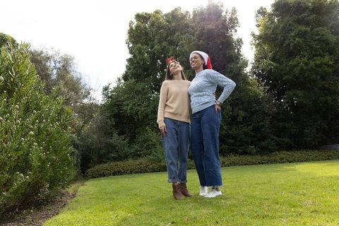 Two friends standing on green lawn wearing santa hat and antler headband celebrating holidays