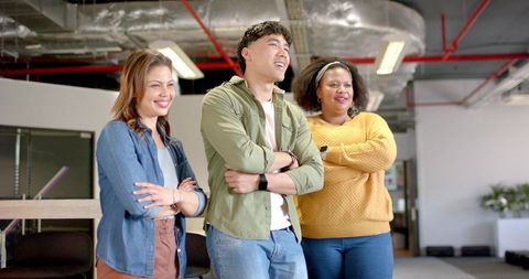 Diverse team standing and smiling in modern open-plan office with industrial ceiling