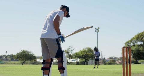 Male cricketer preparing to bat during sunny outdoor practice on grassy pitch with stumps