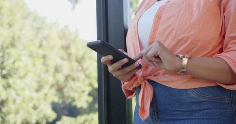 Casual Woman Using Smartphone Next to Glass with Nature View