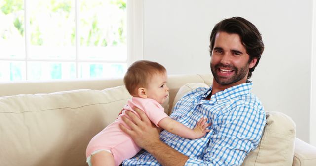 Smiling Father Holding Baby on Couch in Bright Living Room - Download Free Stock Images Pikwizard.com