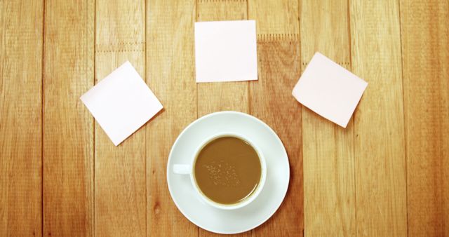 A coffee cup sits on a wooden table next to three blank sticky notes. Ideal for uses related to planning, productivity, and workspaces in both home and office settings. Can be used for articles or advertisements focusing on organization, brainstorming ideas, or work-from-home environments.