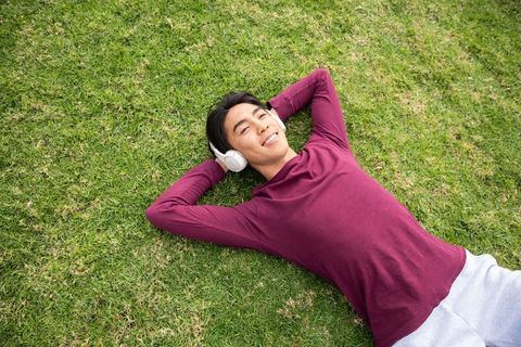 Asian man lying on grass listening to music with headphones feeling relaxed