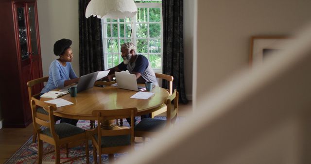 African american couple sitting at dining table using laptops paying bills. staying at home in isolation during quarantine lockdown.