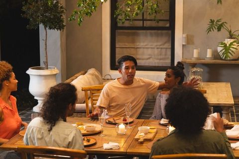 Diverse friends enjoying candlelit alfresco dinner on wooden patio table at dusk